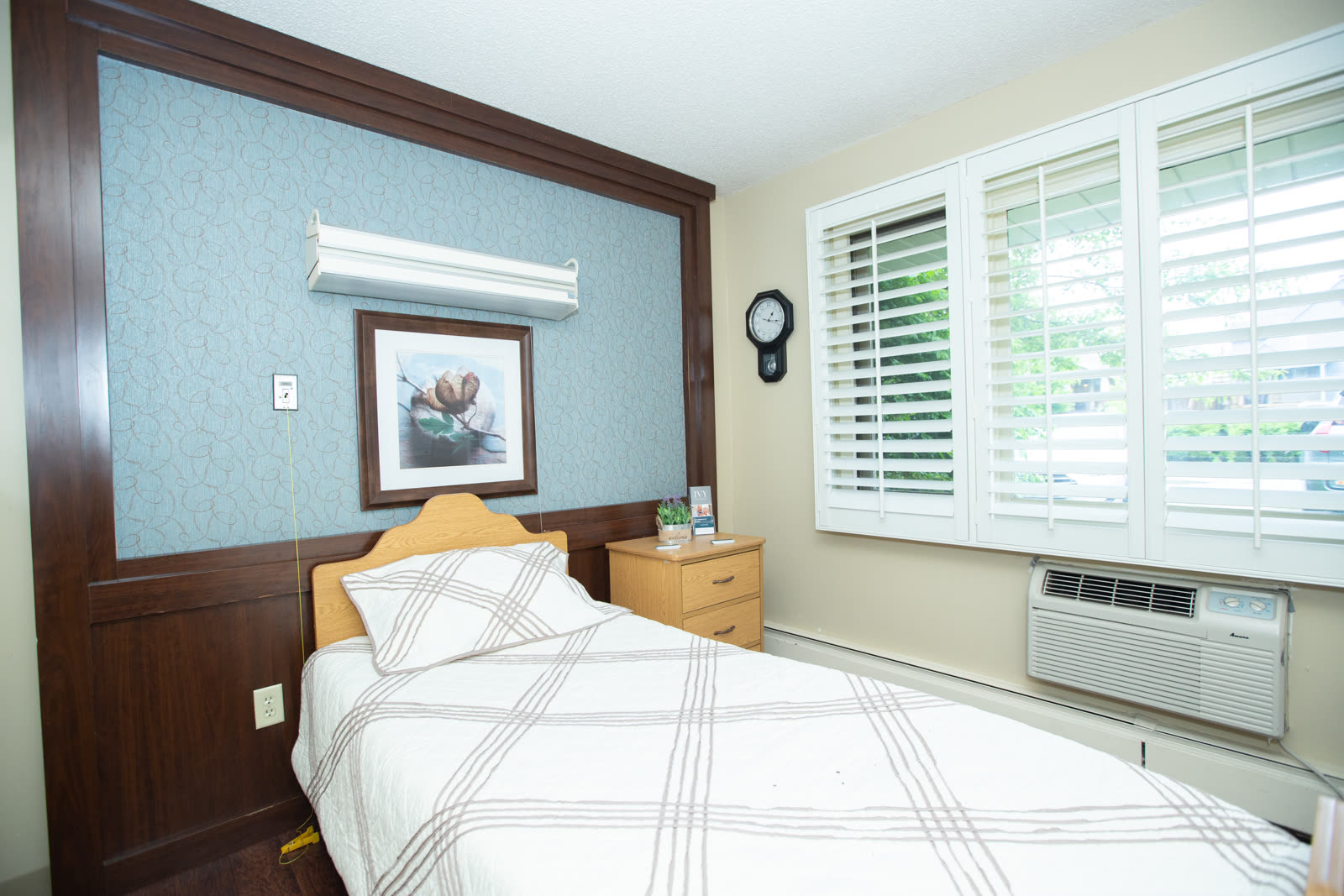 A comfortable private resident room with a neatly made bed and cozy seating area